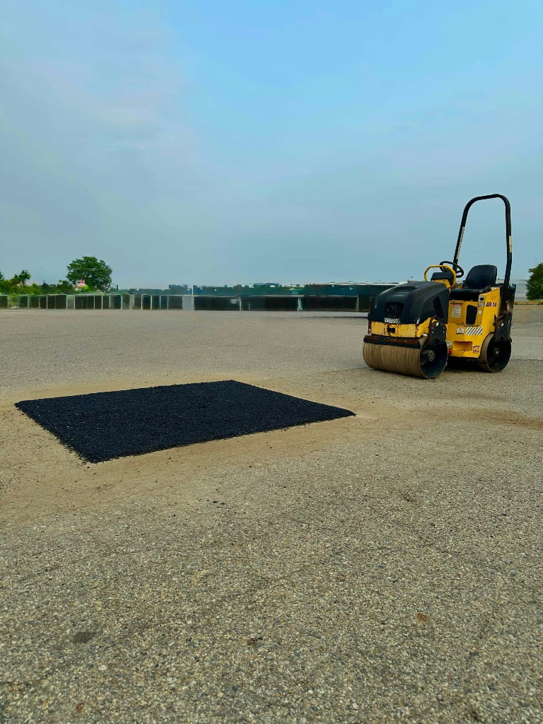 Roller compacting a fresh asphalt patch on a parking lot in Norton Shores, Michigan by Phillip Thomas Excavating (PTE).