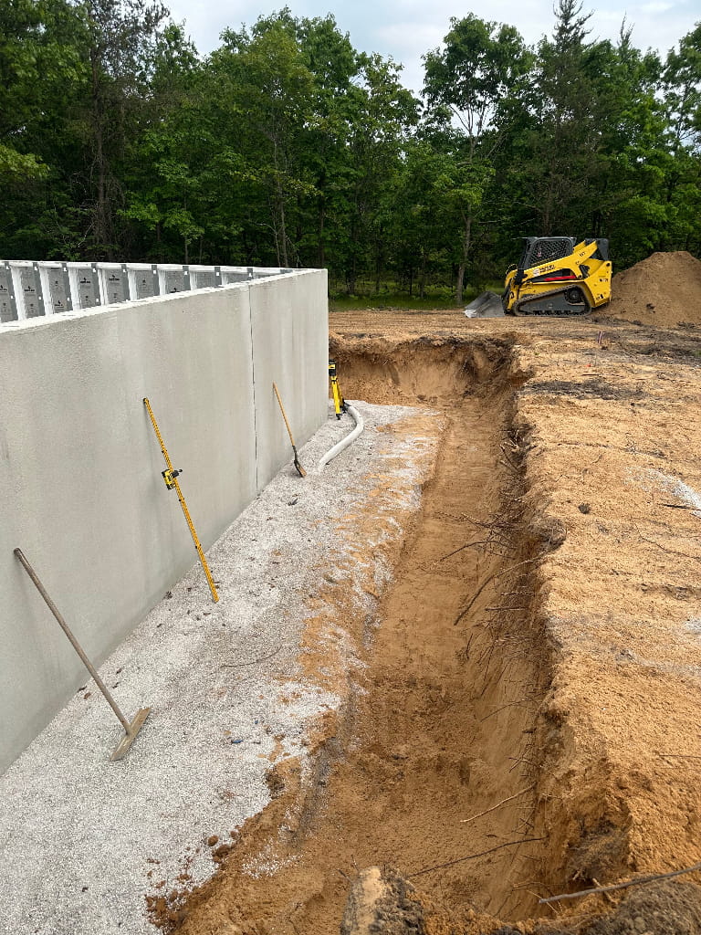 Excavation and backfill prep along a new concrete foundation wall with skid steer on site in Norton Shores, Michigan by Phillip Thomas Excavating (PTE).